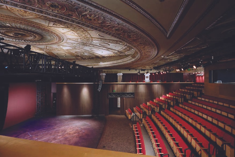 Interior of a theater with ornate ceiling and empty red seats.