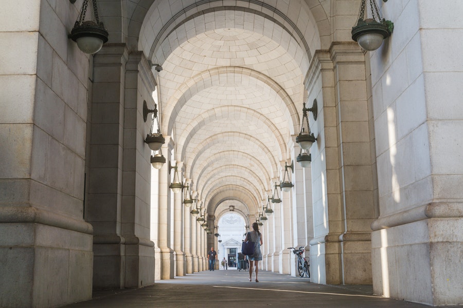 Pedestrians walk beneath the arched colonnade outside Union Station, framed by hanging lanterns and limestone pillars.