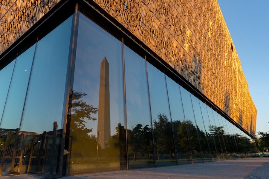 The Washington Monument reflected in the glass exterior of the National Museum of African American History and Culture at sunset.