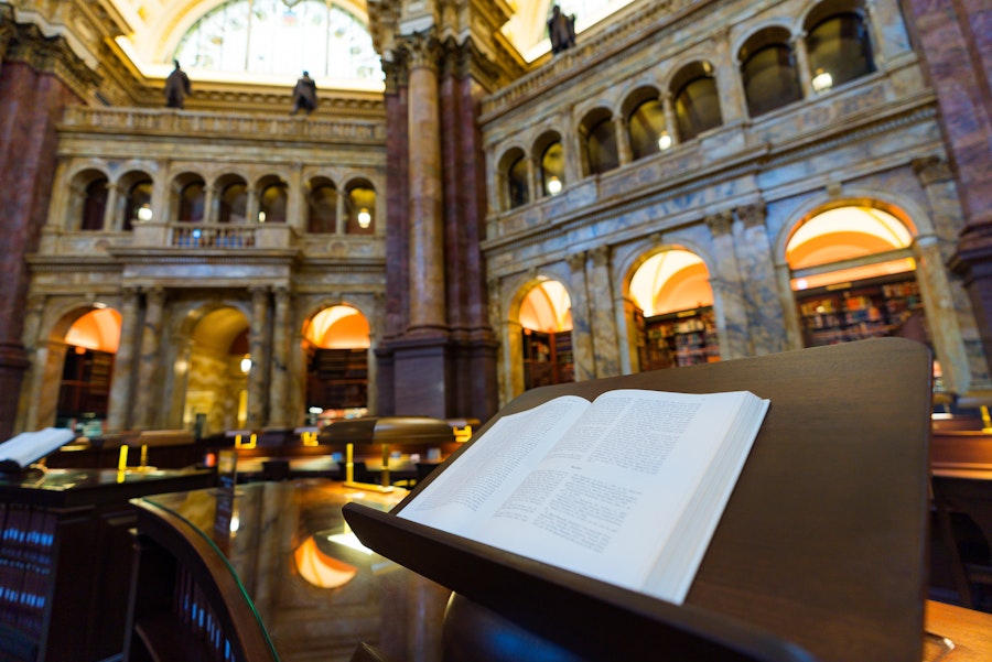 An open book rests on a lectern inside the ornate reading room of the Library of Congress.