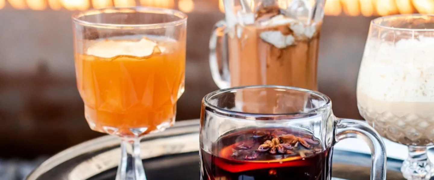 A collection of cozy winter cocktails on a plater in front of a fire. 