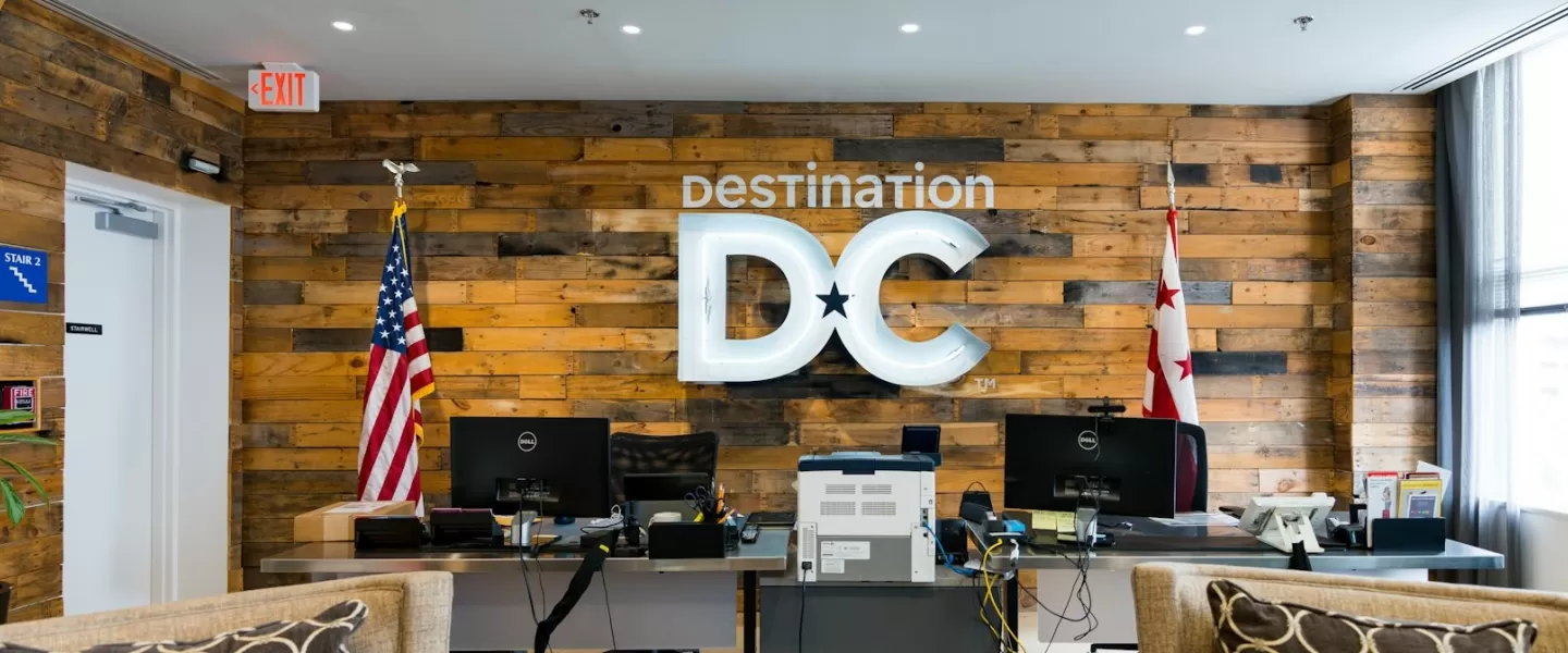 Destination DC front desk with illuminated sign, wooden wall backdrop, and American and DC flags on either side.