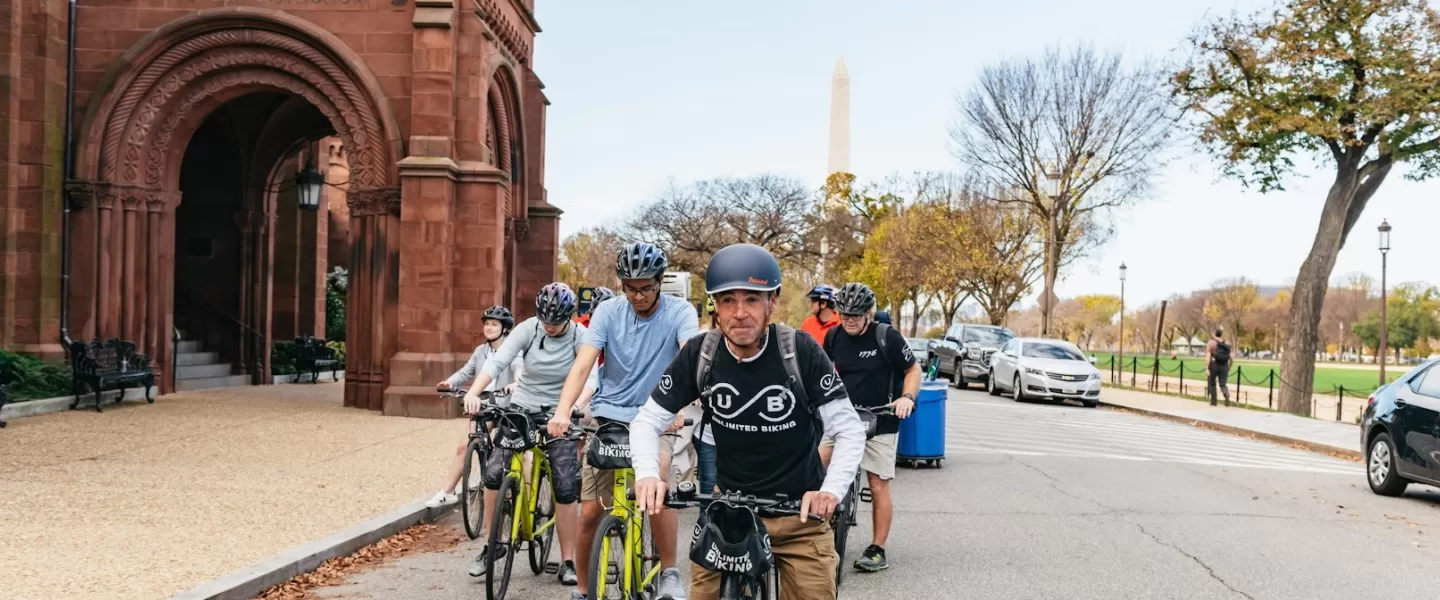 A guide leads a biking tour along the National Mall with the Smithsonian Castle and the Washington Monument in the background. 
