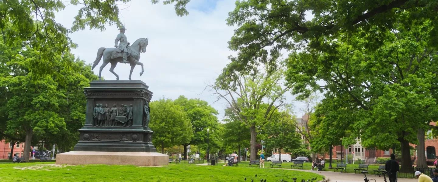 The Logan Circle equestrian statue stands prominently against a backdrop of lush trees and sky, surrounded by benches and walking paths.