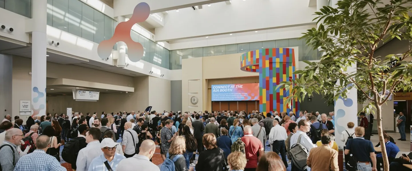 A large crowd of conference attendees gathers in a bright, spacious convention center lobby with colorful signage and modern architectural elements.