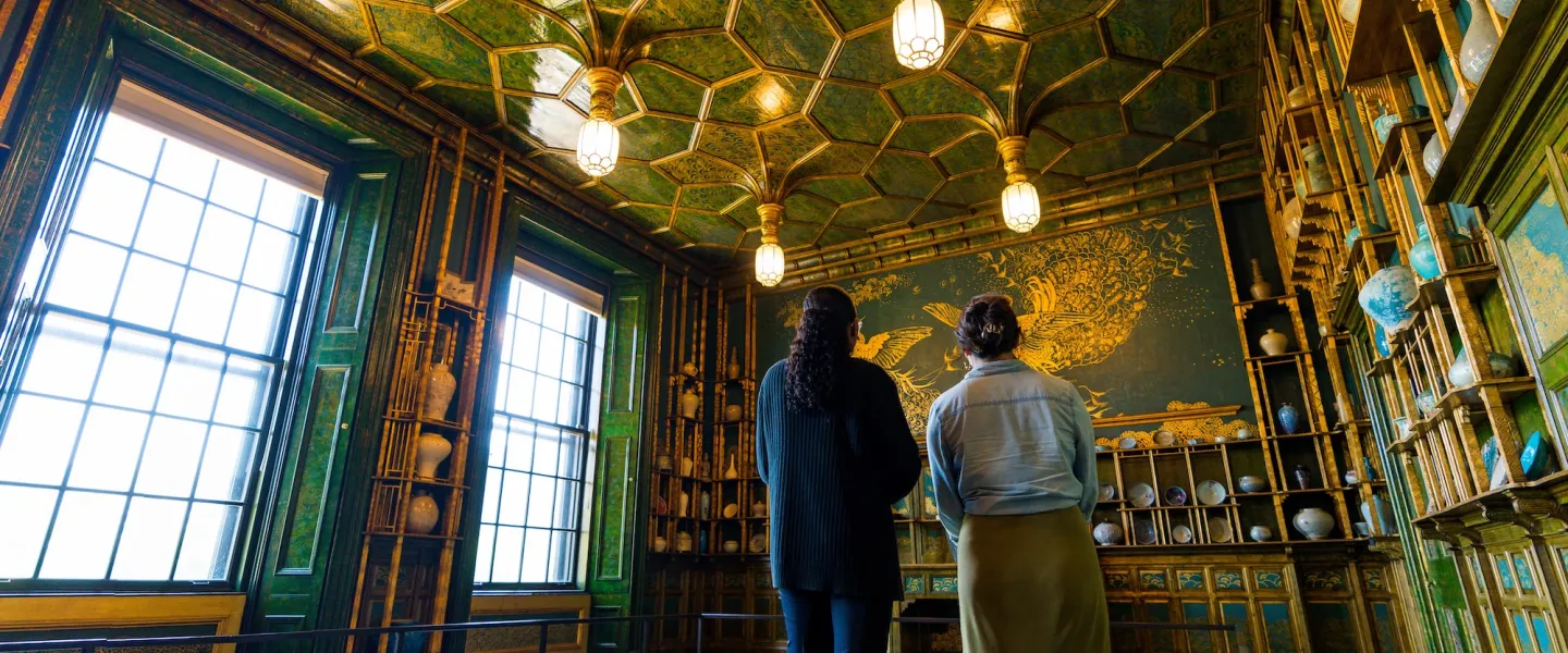 Two people view the ornate green-and-gold Peacock Room filled with ceramics at a museum in Washington, DC