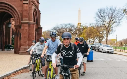 A guide leads a biking tour along the National Mall with the Smithsonian Castle and the Washington Monument in the background. 
