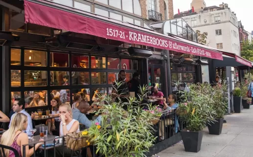 Diners enjoy outdoor seating at Kramerbooks & Afterwords Café in Dupont Circle as pedestrians stroll past the bustling sidewalk café.
