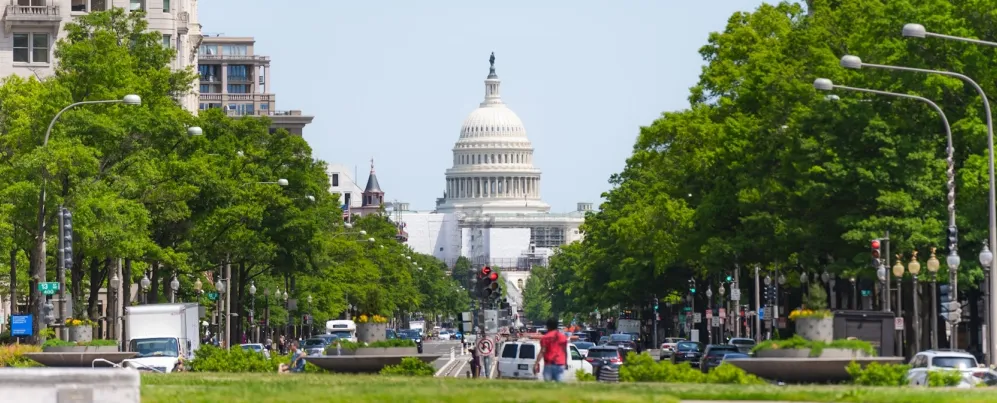 A wide view of Pennsylvania Avenue, lined by trees and leading toward the U.S. Capitol Building.