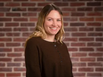 A smiling woman with blonde hair, standing in front of a brick wall.